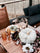 Fall-themed outdoor table with amber glasses, brass accents, and a pale pumpkin centerpiece surrounded by flowers, with a cat resting on a dark cushioned bench in the background