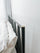 Close-up of black metal bed frame headboard with slim vertical spindles and a rounded wood-accent cap, shown beside white pillows against a light wall to emphasize sturdy construction, modern design, and smooth finish details
