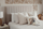 Upholstered bed with a vertically channeled beige headboard, layered white and striped pillows, and a textured quilt, styled with woven wall decor and a plush toy to highlight soft materials, relaxed comfort, and a calm, family-friendly bedroom setting