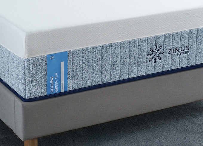 Close-up of Zinus Cooling Green Tea Hybrid mattress with white top and blue patterned side panel, displayed on upholstered bed frame