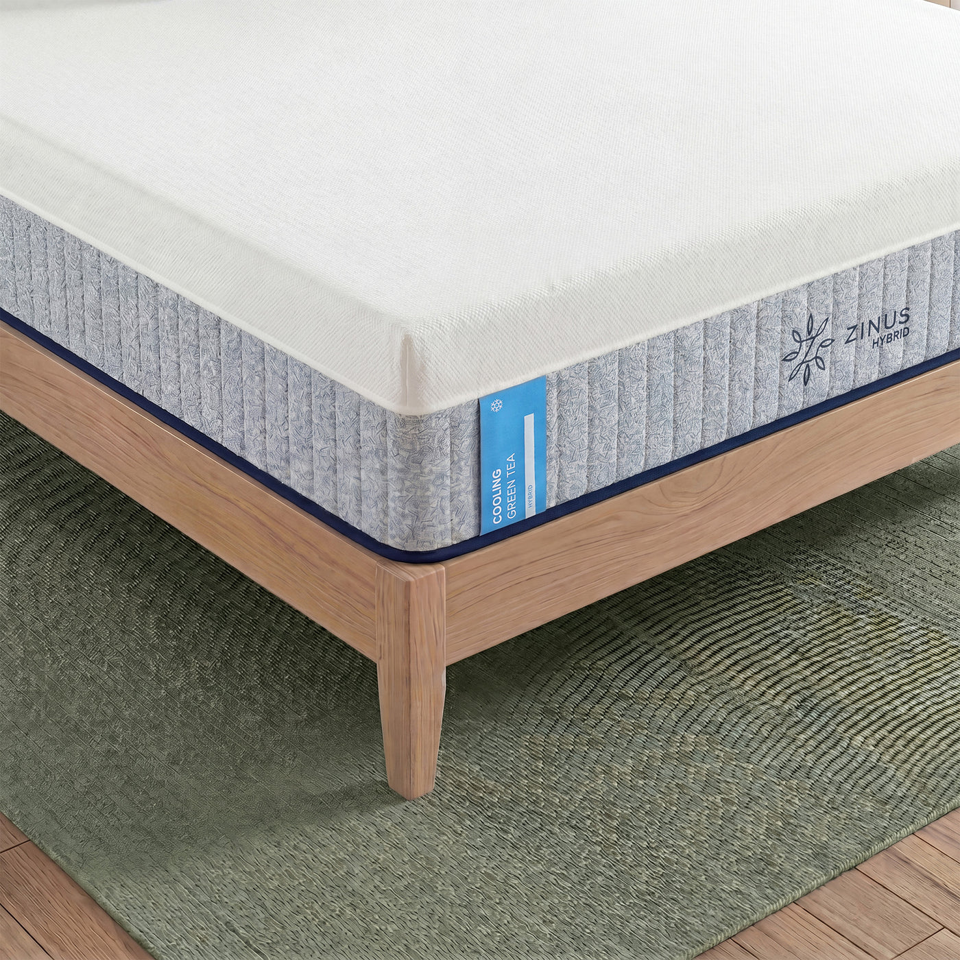 Zinus Balanced Comfort Signature Hybrid Mattress, close-up corner view showing the white knit top cover, channel-quilted gray woven side panel, and Zinus Hybrid brand tag with a cooling icon, set on a natural wood platform bed frame with clean edge stitching.