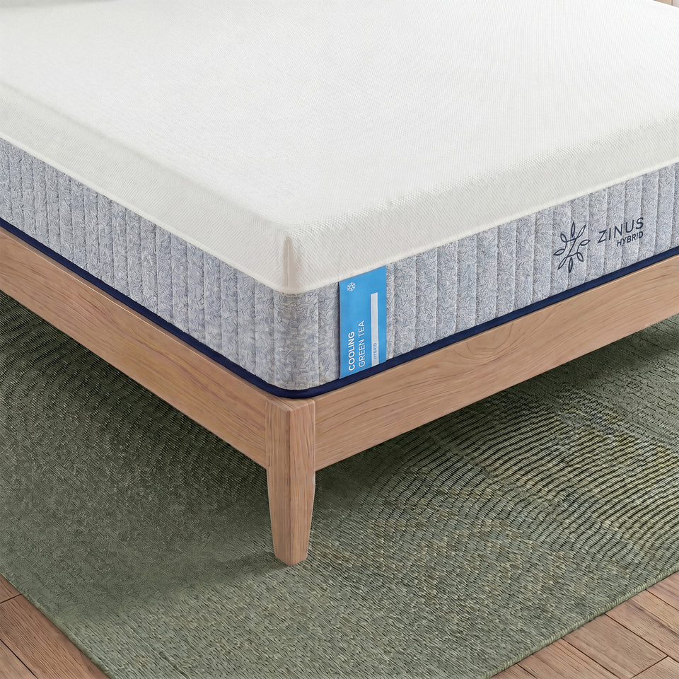 Zinus Balanced Comfort Signature Hybrid Mattress, close-up corner view showing the white knit top cover, channel-quilted gray woven side panel, and Zinus Hybrid brand tag with a cooling icon, set on a natural wood platform bed frame with clean edge stitching.
