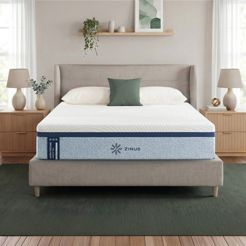 Zinus Balanced Comfort Luxe Memory Foam Mattress fully set up on an upholstered platform bed with wingback headboard in a bright bedroom with white and green pillows, nightstands, and lamps on either side, showing the mattress in its intended home setting.
