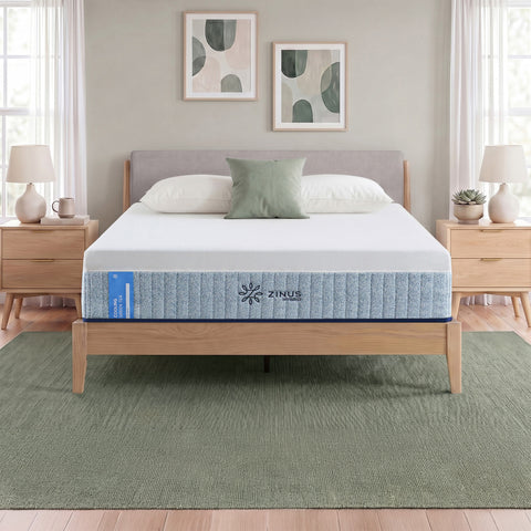 Zinus Balanced Comfort Signature Hybrid Mattress fully set up on a natural wood platform bed with upholstered headboard in a light bedroom with white and green pillows, nightstands, and lamps on either side, showing the mattress in its intended setting.