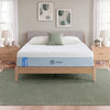 Zinus Balanced Comfort Signature Memory Foam Mattress fully set up on a natural wood platform bed with upholstered headboard in a light bedroom with white and green pillows, nightstands, and lamps on either side, showing the mattress in its intended setting.