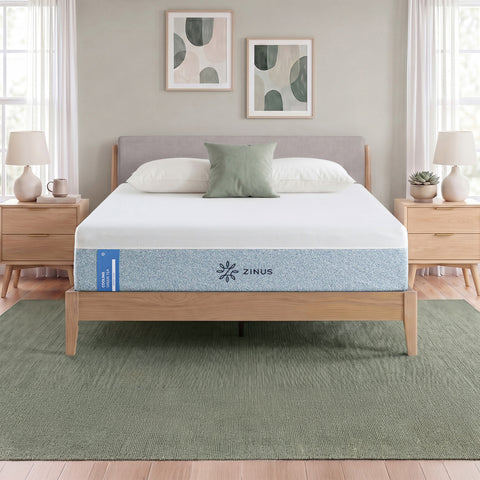 Zinus Balanced Comfort Signature Memory Foam Mattress fully set up on a natural wood platform bed with upholstered headboard in a light bedroom with white and green pillows, nightstands, and lamps on either side, showing the mattress in its intended setting.