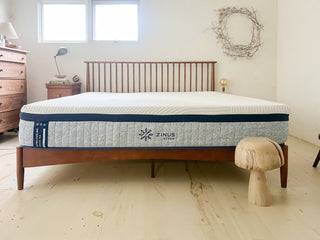 Zinus Ultra Cooling Green Tea Hybrid mattress with white top and gray patterned side panel on wooden slat bed frame, shown in a bright bedroom with wood dressers, neutral decor, and natural light, highlighting breathable cooling support in a clean modern-rustic style.