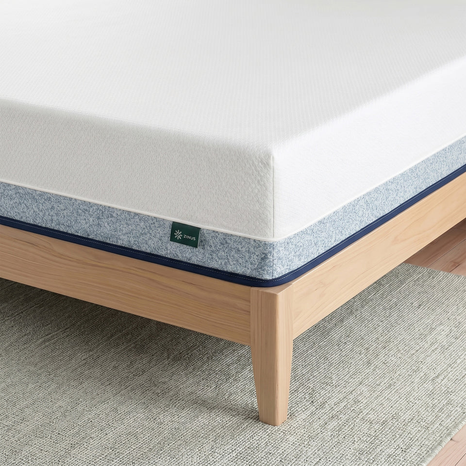 Zinus Original Green Tea Hybrid Mattress, Queen, close-up corner detail showing white knit top cover, gray textured side panel with navy piping, and Zinus logo tag, resting on light wood platform bed frame.