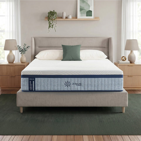 Zinus Ultra Cooling Green Tea Hybrid Mattress, Queen, on upholstered bed frame in bright bedroom with white pillows, sage cushion, plants, wall shelf decor, and matching nightstands with lamps.