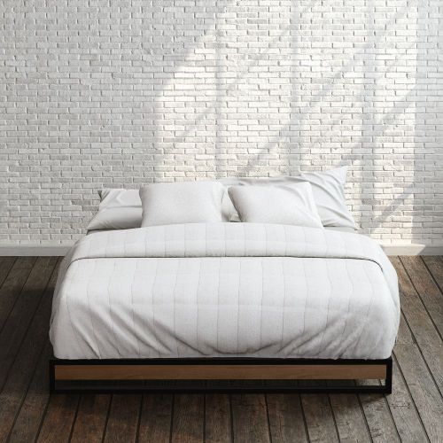 Zinus Suzanne Metal and Bamboo Platform Bed Frame in queen size, styled with white bedding against a brick wall backdrop. Black steel frame with bamboo accent panel and slatted base offers sturdy support and a clean, modern look for any bedroom.